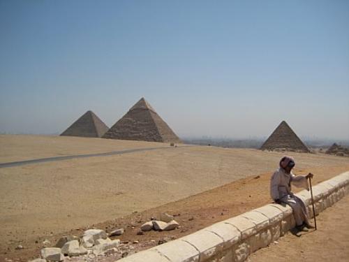 Man sitting on rock wall with pyramids in the distance