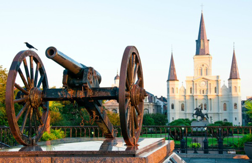 A bronze canon guards the famed Jackson Square of New Orleans French Quarter. In the background rises St. Louis Cathedral—a beautiful building standing like a Disney castle. 