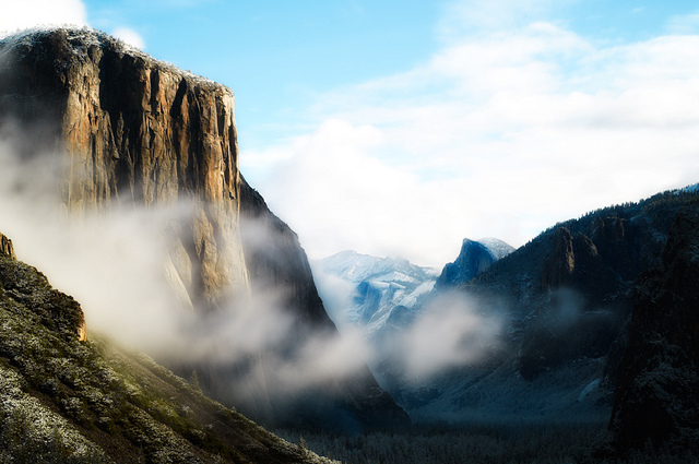 Mist wafts through a valley in Yosemite National Park, surrounded by mountains and rock formations.