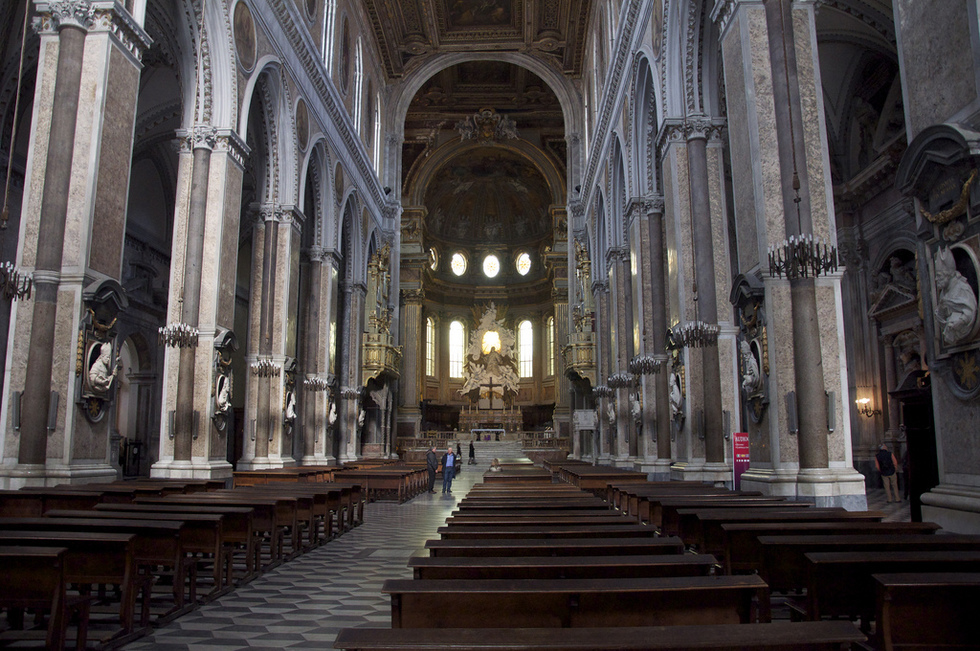 The interior of a cathedral with pews, massive columns and tile floors. 