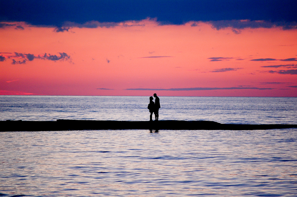 A couple walking down the beach with a pink sunset behind them. 