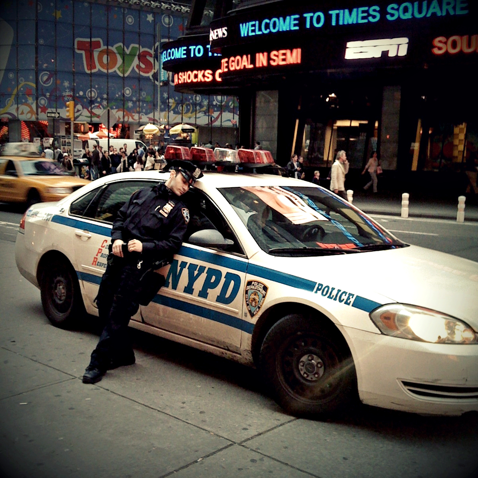 A NYPD officer rests against his car in Times Square