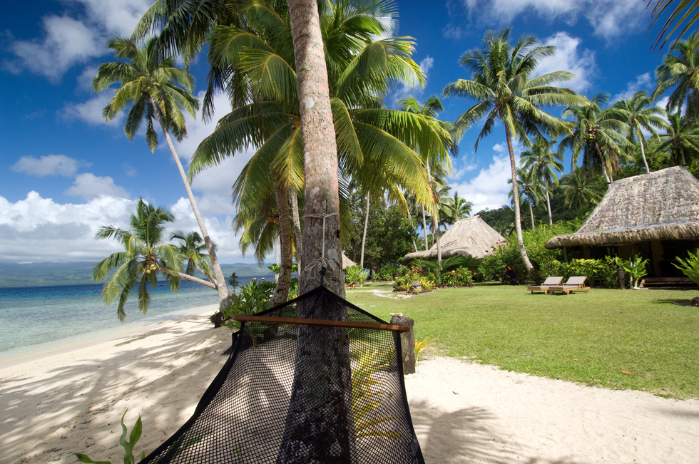 A hammock resting between trees on a white sand beach