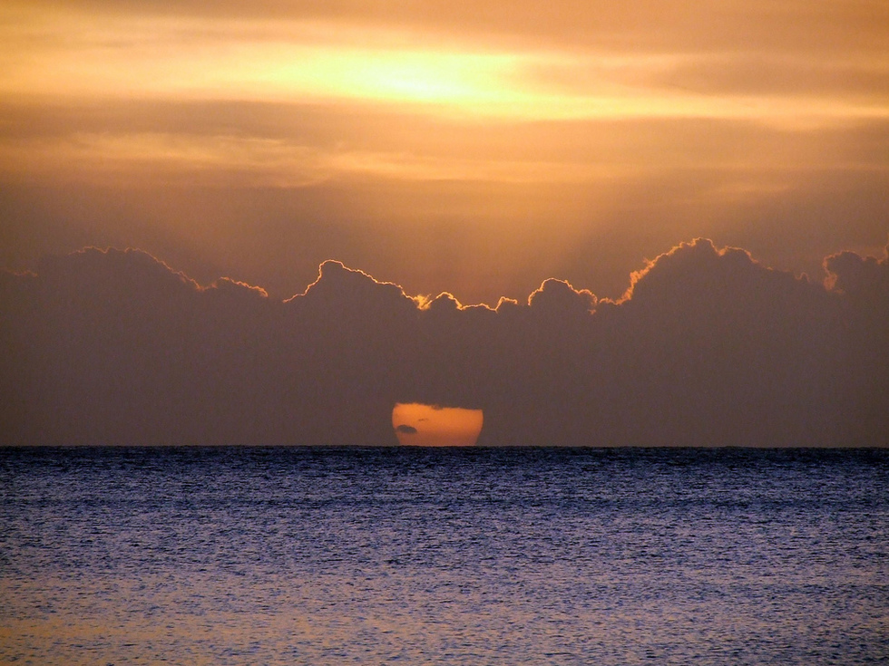 A sunset over the ocean with an orange halo surrounding the clouds. 