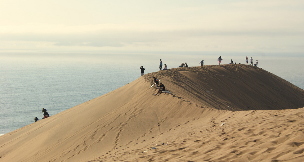 People sandboarding down a dune in Chile