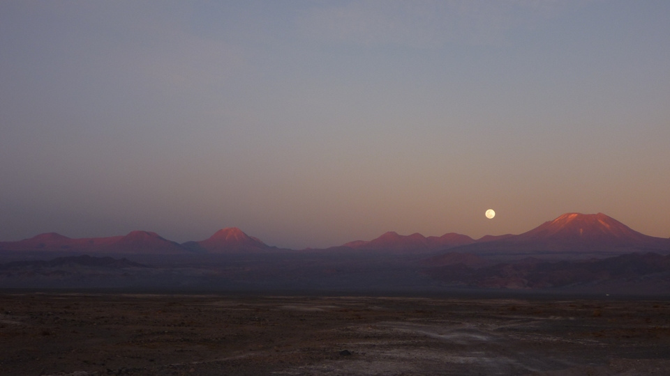 The moon appearing over mountains in the Atacama Desert as the last light from the sun fades