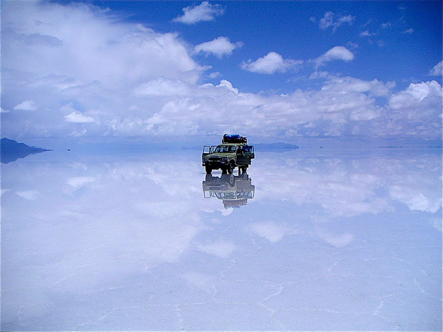 A tourist jeep stopped in the middle of Salar de Uyuni, which is covered in a layer of water and reflecting the skies above