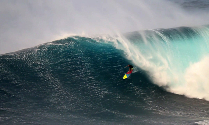 A surfer is challenged by a massive wave