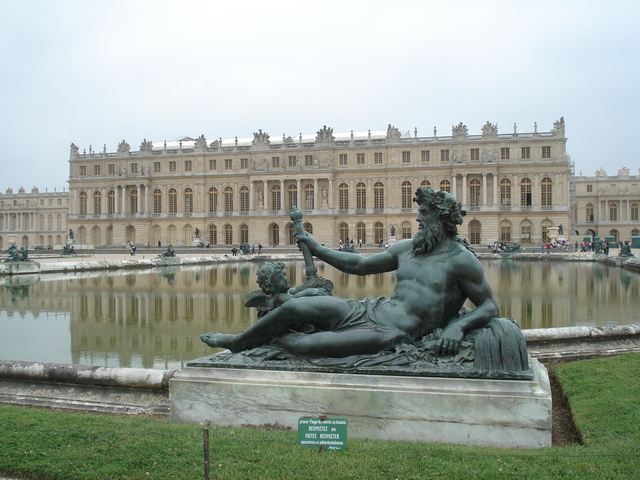 A closeup of the four bronze statues with the Palace of Versaille in the background. 