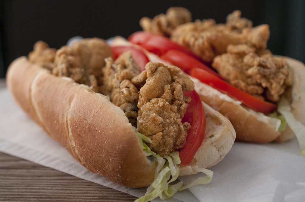A closeup of a fried oyster sanwich on a bun with lettuce and tomato. 