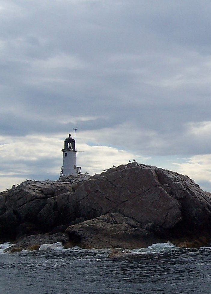 Shot of white lighthouse on big rocky island on overcast day