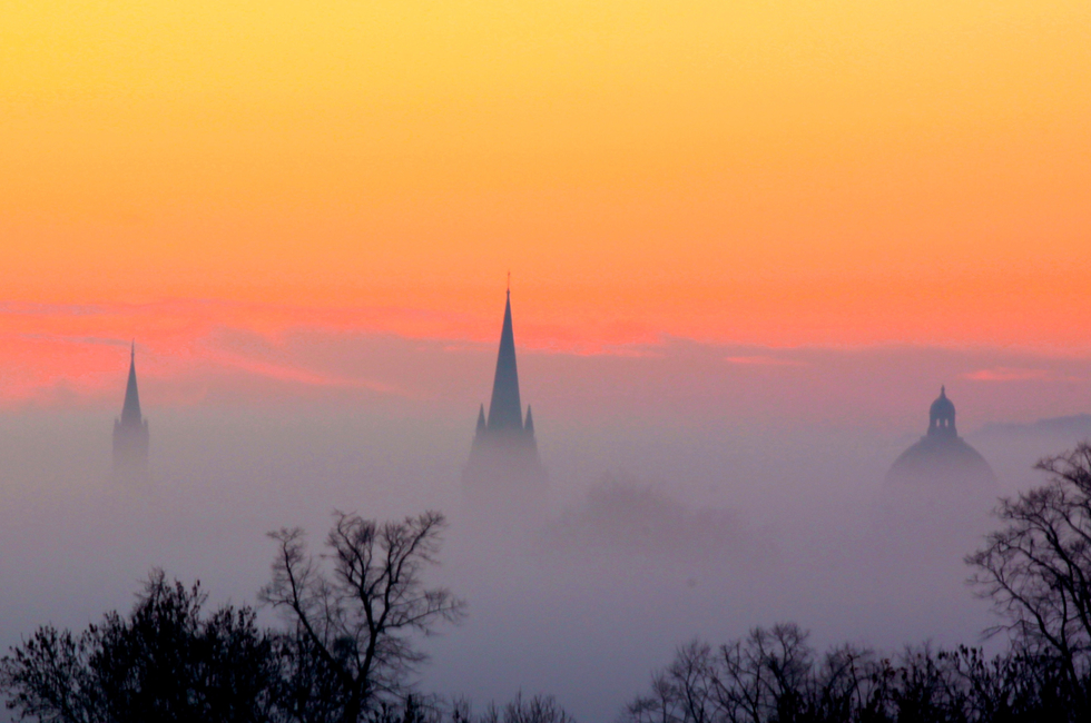 Oxford dreaming spires against orange cloudy sky with tree silhouettes