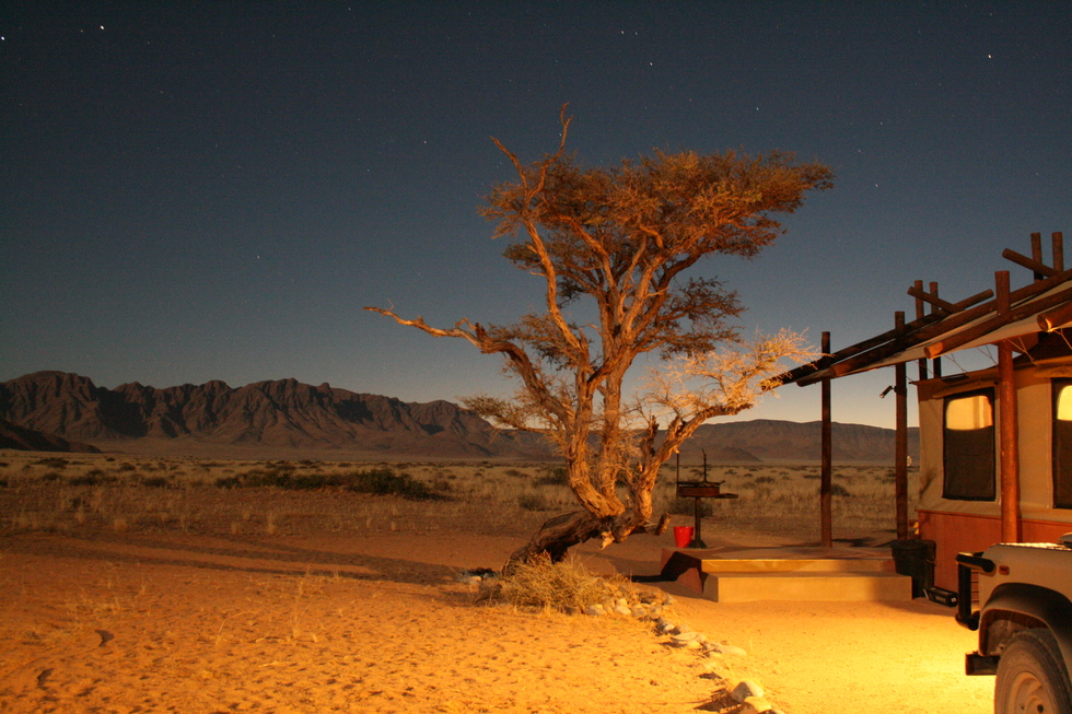 Cabin at desert camp lit up against backdrop of ethereal desert night sky
