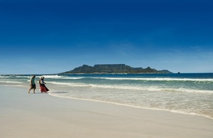 A couple walks along Blouberg Beach in Cape Town, with Table Mountain in the background