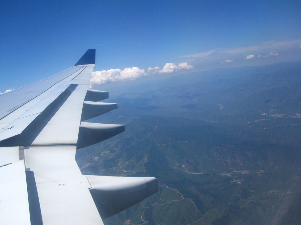 An airplane wing soars over a mountainous landscape
