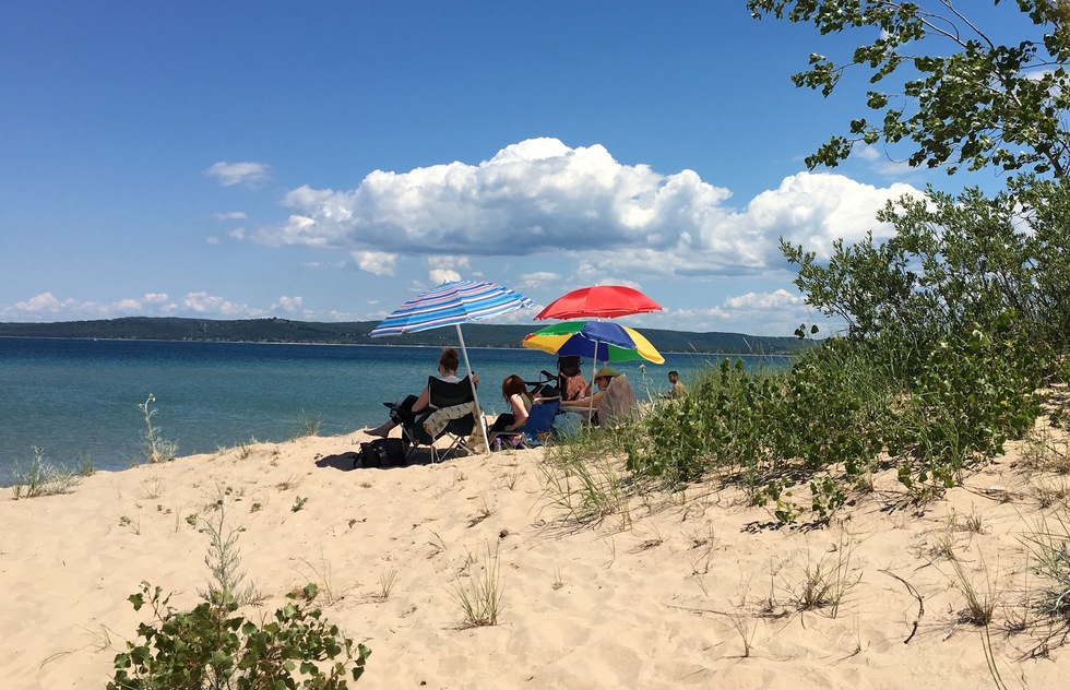 Vacationers sit under colorful beach umbrellas on the beach at Mission Point Park.