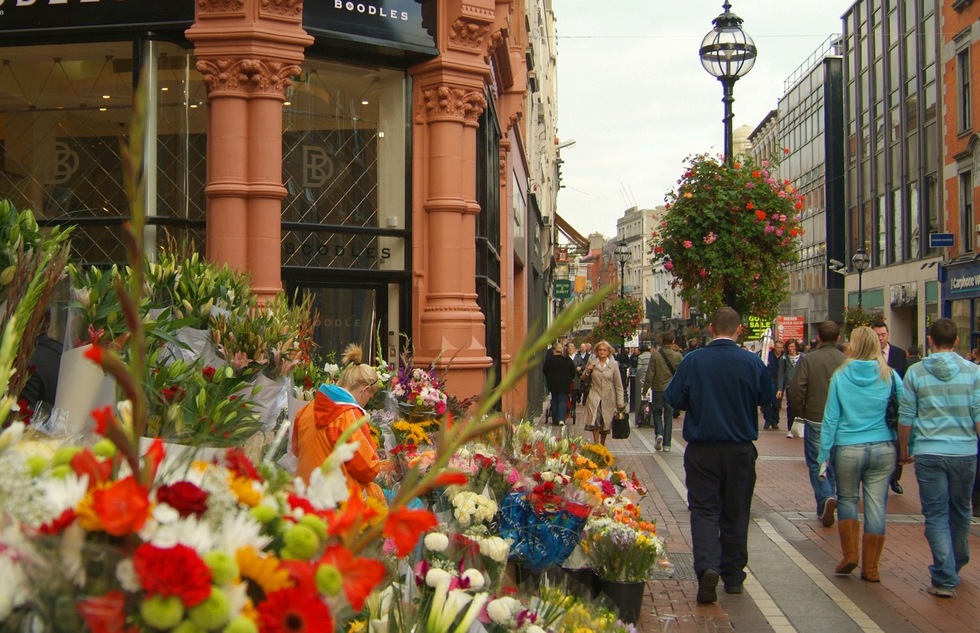 Pedestrians stroll past shops and flowers for sale on Grafton Street in Dublin