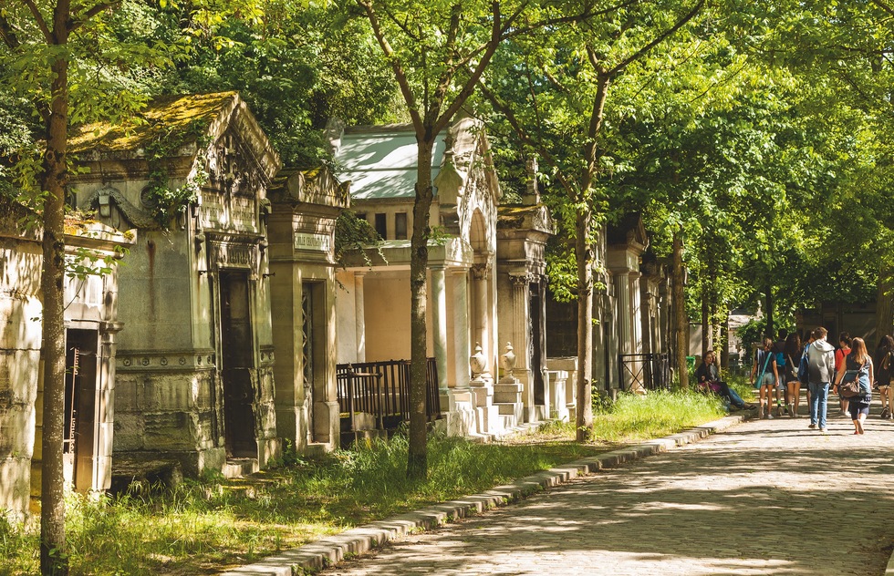 Visitors stroll past crypts along a leafy walkway in Père-Lachaise cemetery in Paris