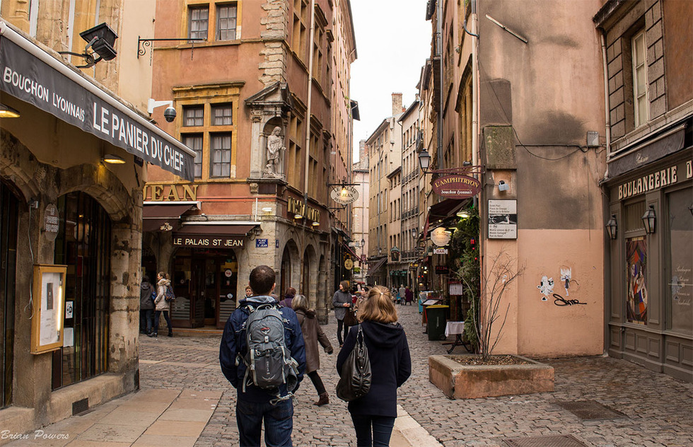 Tourists and locals walking a cobble-stoned street of Vieux Lyon with several Lyonnais bouchons, boulangeries, and restaurants