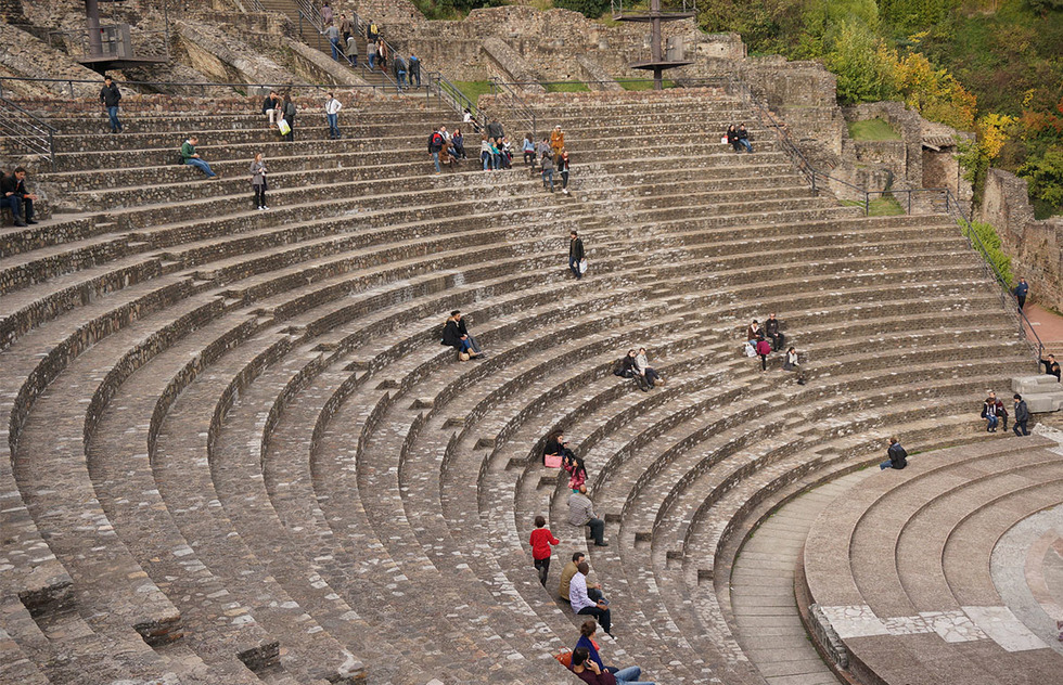 A crowd of visitors exploring and sitting in the stone stands of the Grand Roman Theatre of Lyon