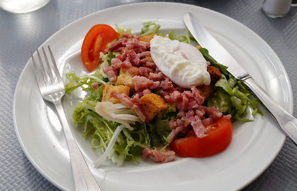 A Lyonnaise salade topped with a poached egg, bacon, tomatoes, croutons, and a Dijon dressing