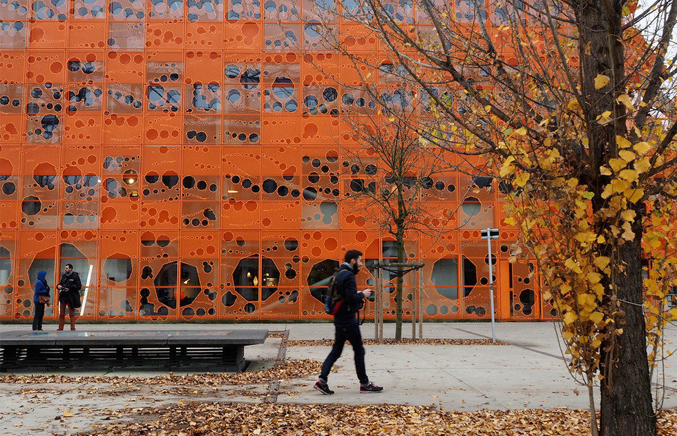 A seven-story neon orange cube with swiss-cheese-like holes cut out for air circulation and light.