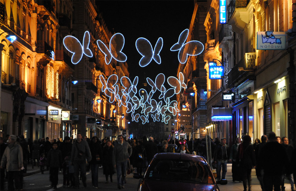 A crowded Lyonnais street at night during the Festival of Lights lined with large lit-up butterfly decorations
