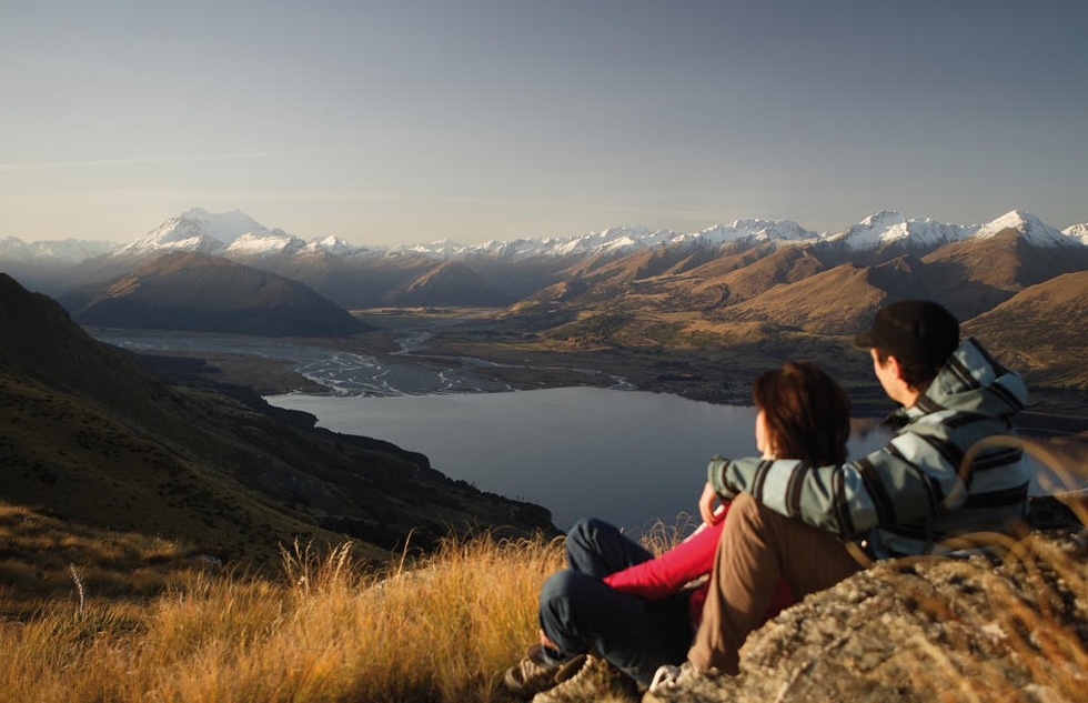 Two hikers overlook Lake Wakatipu and the surrounding snow-capped mountains in Queenstown, New Zealand
