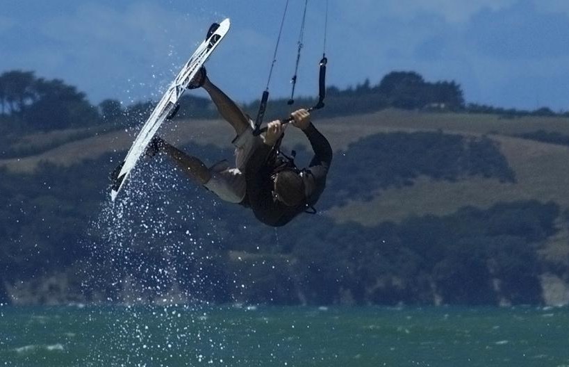 A kiteboarder hangs upside down over water in New Zealand.