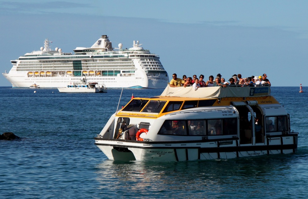 A small ship tenders passengers to shore from a big cruise ship