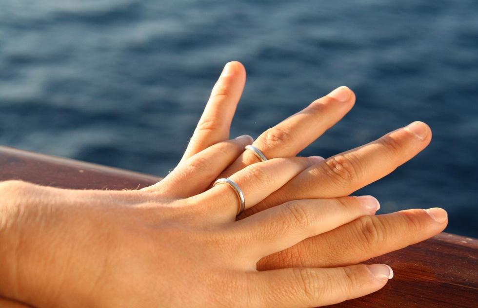 Hands with wedding rings on the railing of a ship