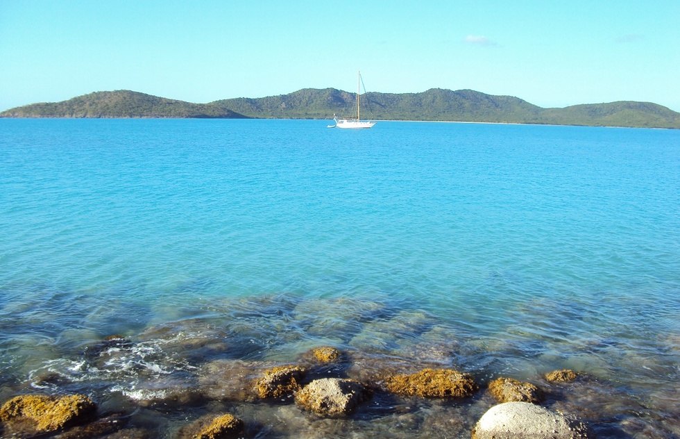 A small boat in open water. Behind it are the rolling hills on the coast of an island.