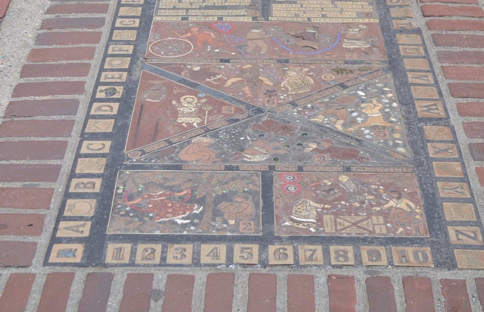 Sidewalk mosaic with pictures of children jumping rope, swinging from trees, and reading.