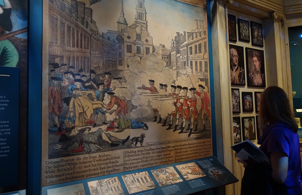 A woman gazes at a blown up poster depicting the Boston Massacre at the Museum of the American Revolution
