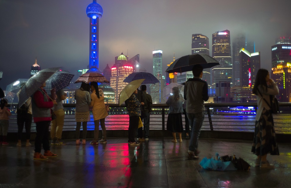 A rainy night in Shanghai. People with umbrellas look at the lit up buildings for the Bund.