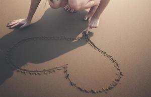 A romantic draws a heart in the sand on a serene beach.