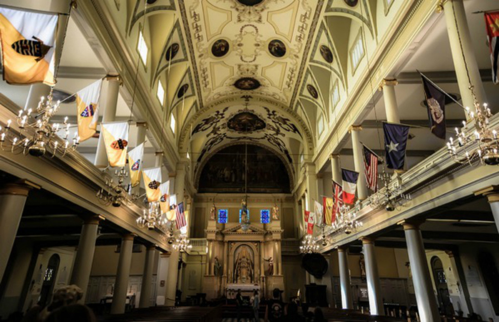 The breath-taking interior of the St. Louis Cathedral features a beautiful vaulted ceiling adorned with small paintings. Balconies run along both sides of the inside with various flags hanging off them.   