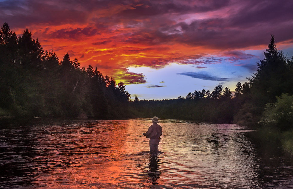 A man fly fishes in the Au Sable river at dawn