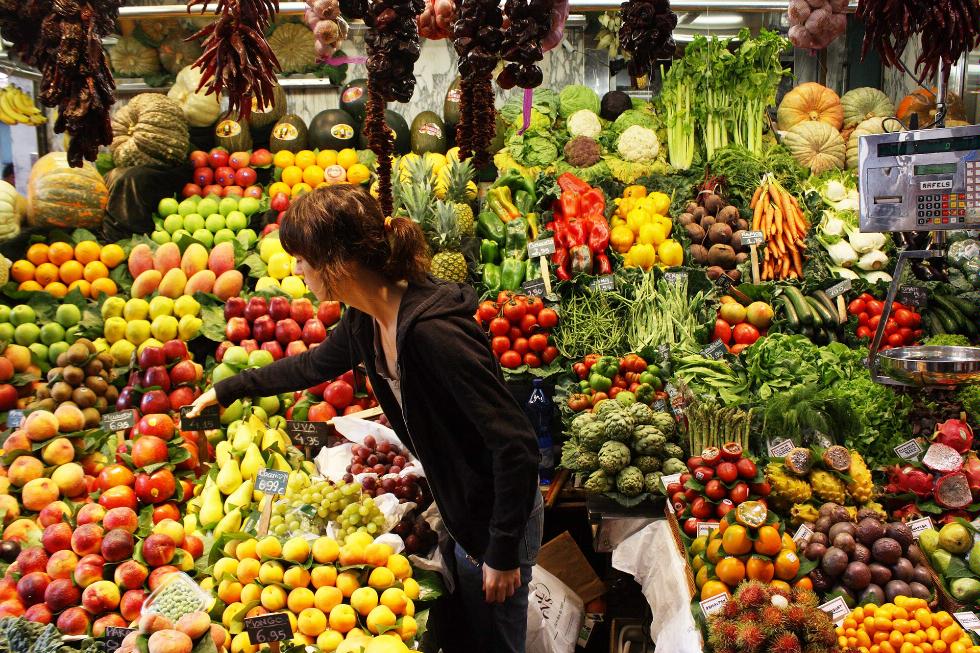 A woman browses a fruit and vegetable stall at the Mercat de La Boqueria, Barcelona, Spain