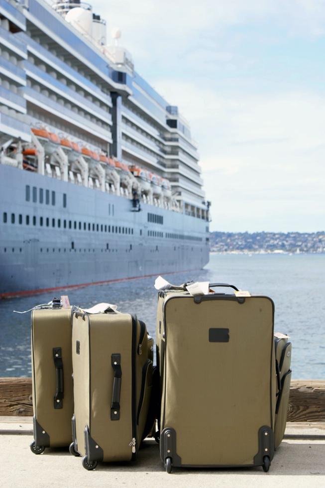 Luggage on the dock next to a cruise ship.
